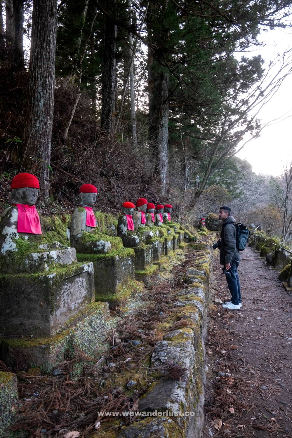 man standing in front of a row of jizo statues at kanmangafuchi abyss in nikko japan